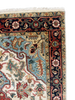 Close-up of an ornate patterned rug corner showing cream, navy, red, and light blue sections with woven floral motifs and a fringed edge.