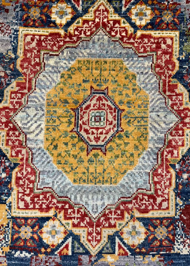 A close-up of a traditional patterned rug with a central medallion design in yellow, red, blue, gray, and cream.