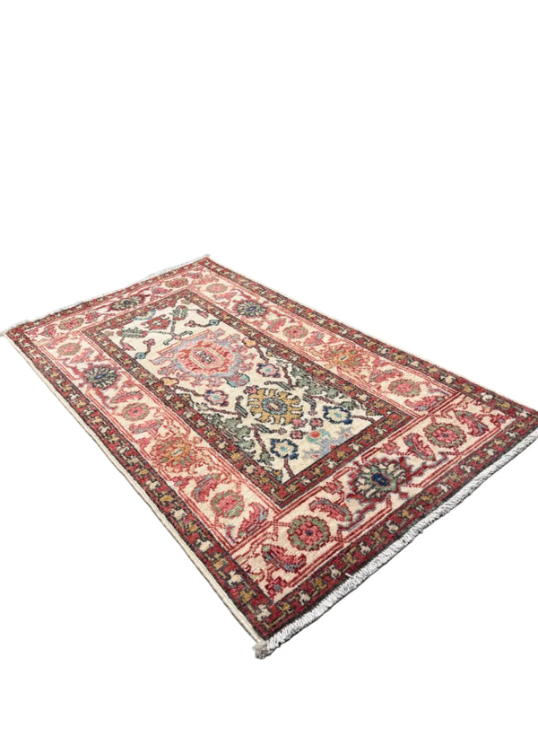 A rectangular Persian-style area rug with a traditional floral and geometric pattern, displayed on a gray concrete floor in a showroom with other rugs rolled up in the background.