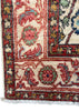 Close-up of an ornate patterned rug corner showing cream ground with red, blue, green, and beige floral motifs and white fringe.