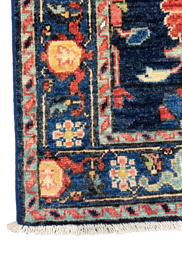 A close-up of a traditional patterned rug corner showing a deep navy blue field with cream, red, and light blue motifs, plus white fringe along the bottom edge.