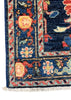 A close-up of a traditional patterned rug corner showing a deep navy blue field with cream, red, and light blue motifs, plus white fringe along the bottom edge.