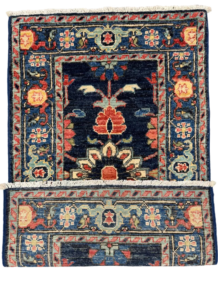 A traditional hand-knotted oriental rug with a dark navy blue field, featuring a central floral motif in red, orange, and cream, surrounded by a detailed patterned border. The rug is shown in two overlapping pieces to display its full rectangular shape and white fringe details, laid flat on a neutral gray concrete floor.