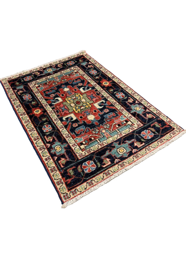 A rectangular patterned area rug with a dark navy blue field, cream borders, and a central medallion in red, beige, and turquoise, photographed on a gray concrete floor.