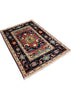 A rectangular patterned area rug with a dark navy blue field, cream borders, and a central medallion in red, beige, and turquoise, photographed on a gray concrete floor.